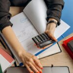 A business professional uses a calculator among documents and laptop on a desk for financial tasks.